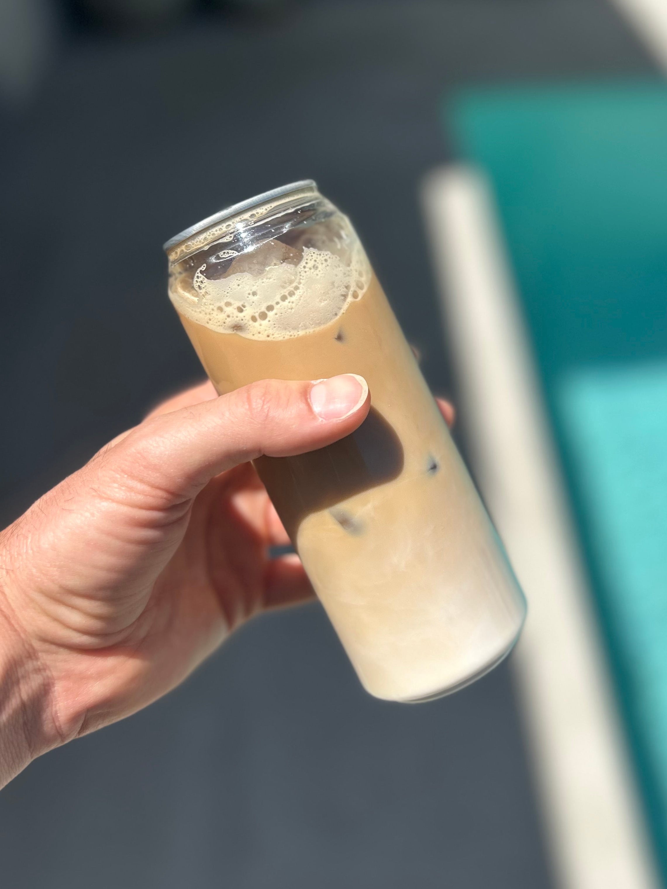 Hand holding a glass of iced coffee with a blurred background